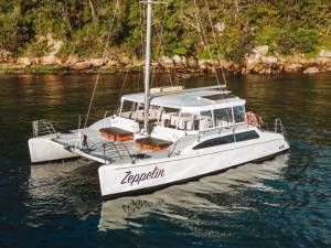 White catamaran named Zeppelin anchored in calm waters near a forested shoreline during week long catamaran cruises