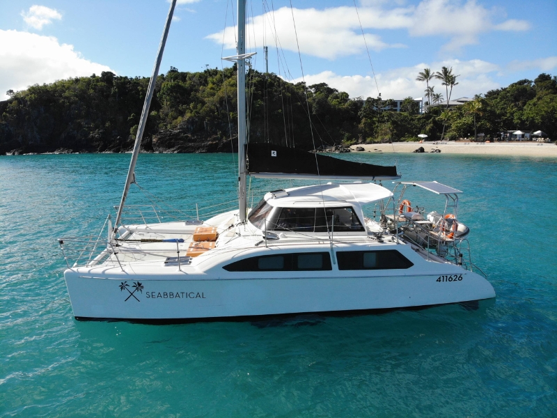 Why Choose a Luxury Catamaran Charter for Special Occasions White luxury catamaran charter anchored in turquoise water near a quiet tropical beach surrounded by lush greenery.